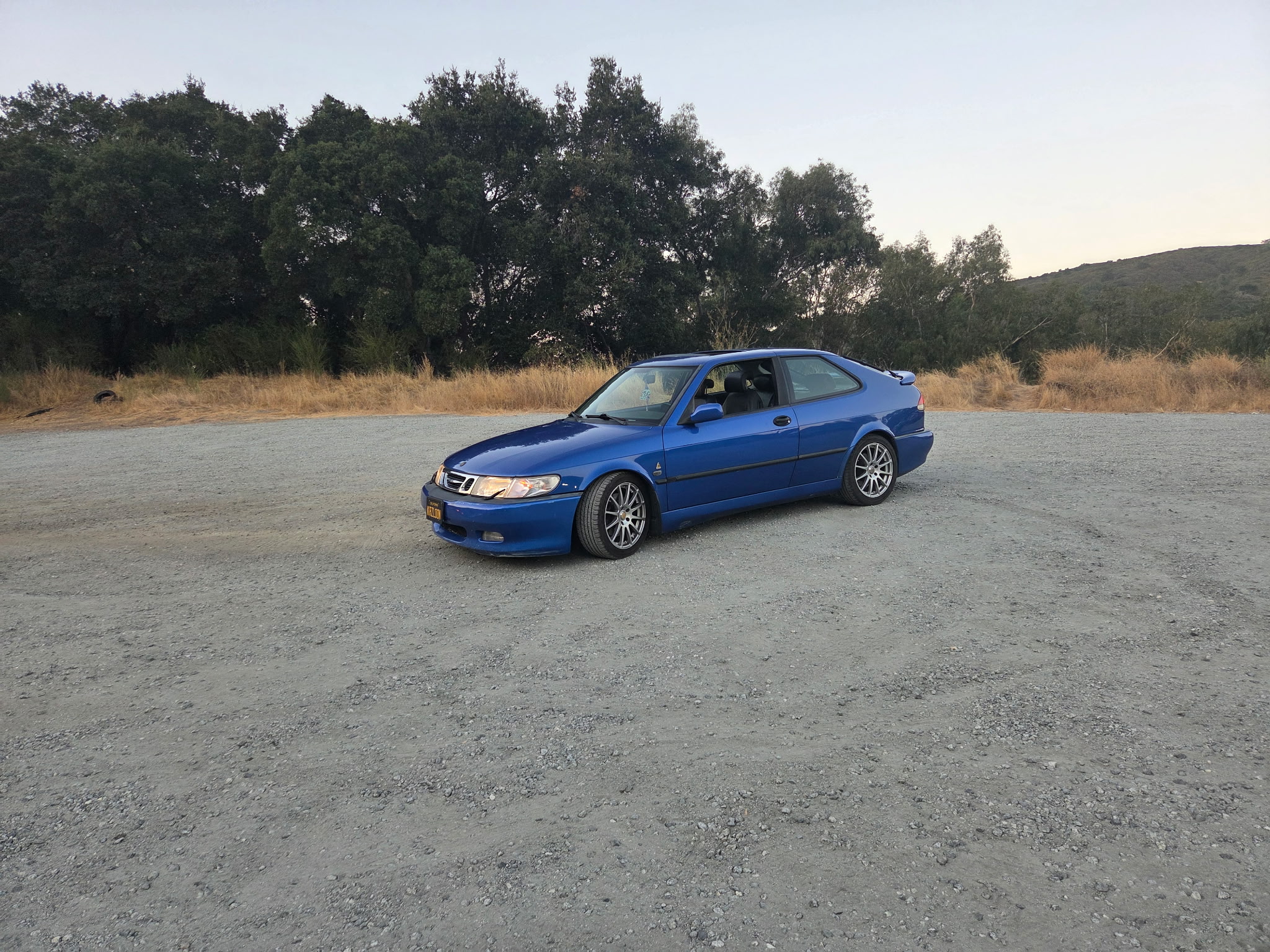 Lightning Blue Saab 9-3 Viggen at a gravel turnout in golden evening light, front three-quarter, plate not legible